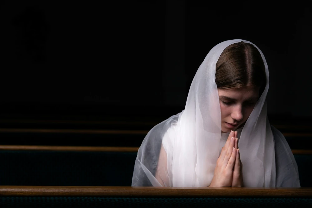 Woman wearing veil praying in Church (Photo by Volodymyr Hryshchenko on Unsplash)